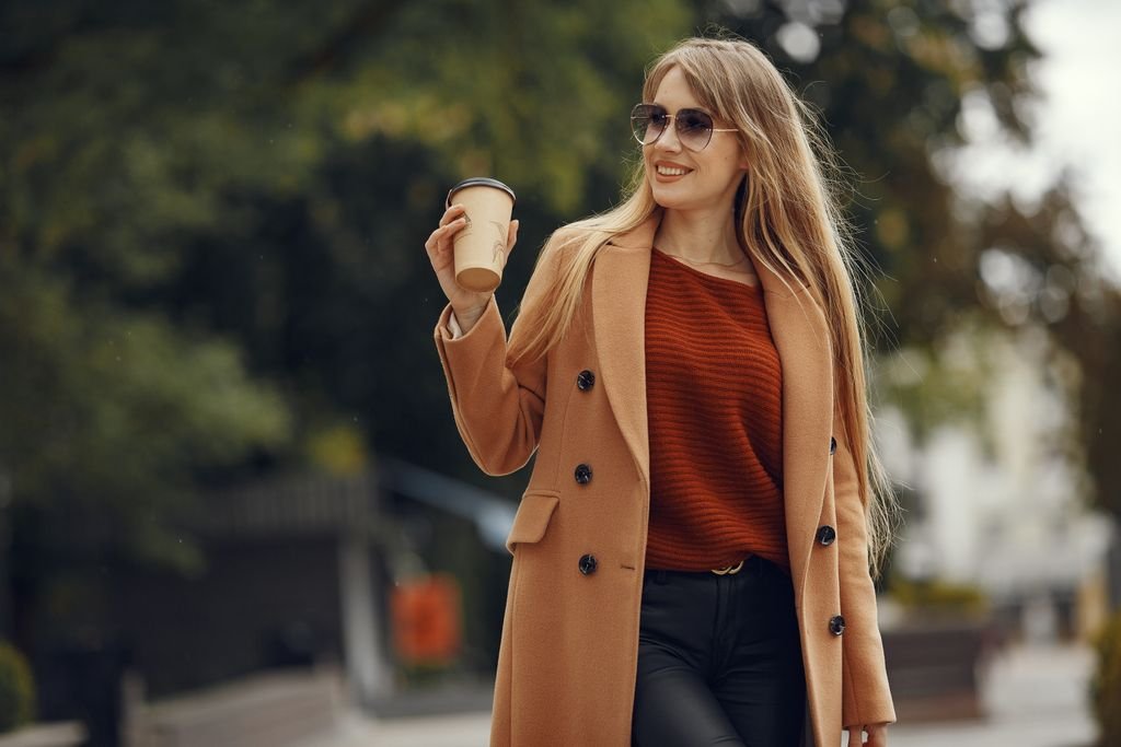 Woman in a fall outfit with a camel coat, knit sweater and ankle boots